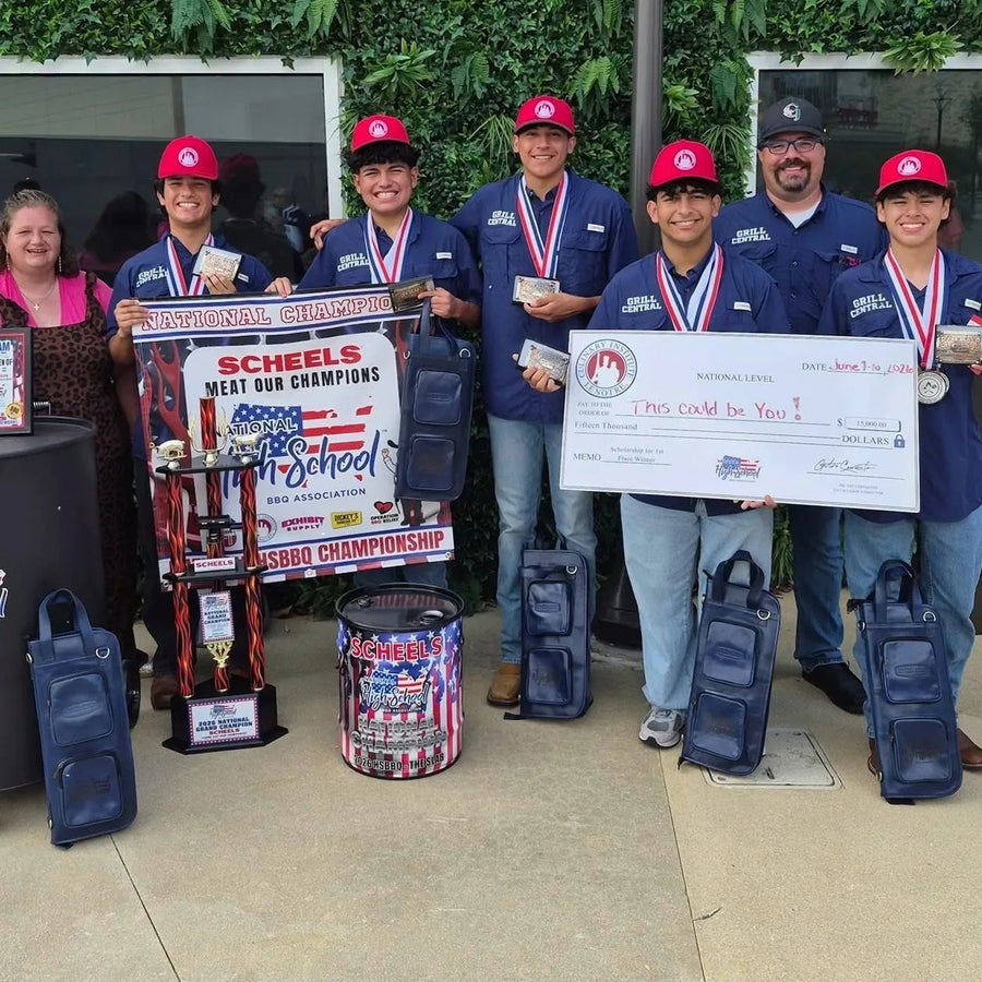 A group of young men wearing matching blue and red athletic uniforms and red caps celebrate with trophies, medals, and a large check on an outdoor patio. Several blue Drumstick Knife bags are placed on the ground around them, and a trophy stand with multiple awards is visible in the center-left.