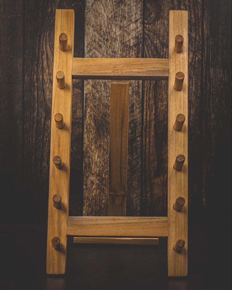 A rustic wooden Knife Tower Standladder-style rack with pegs on the sides, photographed against a dark wood plank background.